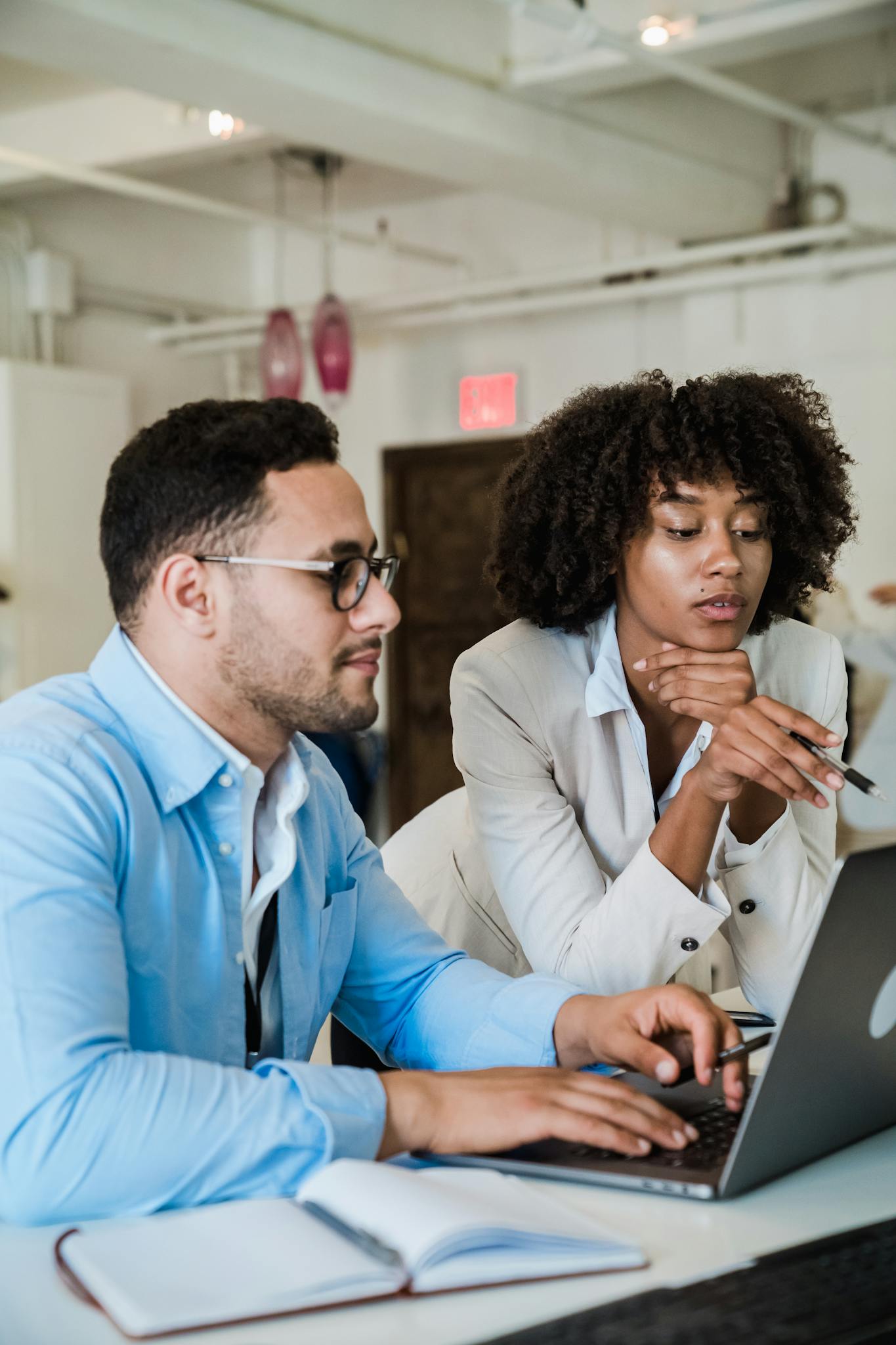 A man and a woman collaborating on a laptop in a modern office setting.